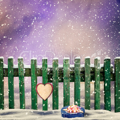 snow-covered wooden fence with a paper heart and a gift