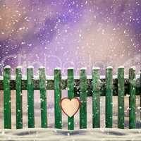 snow-covered wooden fence with  paper heart