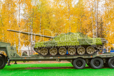 Tank under camouflage network on truck platform