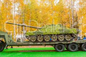 Tank under camouflage network on truck platform