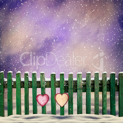 snow-covered wooden fence with two paper hearts