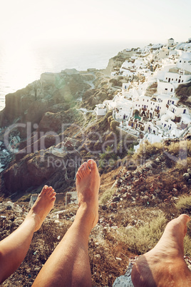 Oia village seen from two people with legs visible in the photo.