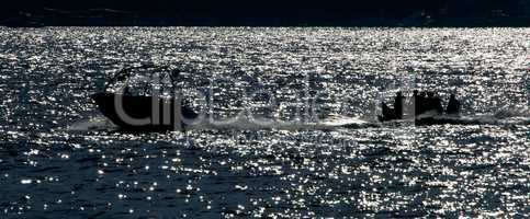 Backlit speedboat pulling inflatable banana at sea