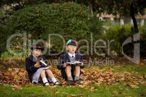 Brother and sister sitting reading among leaves