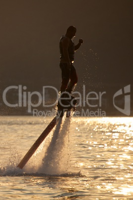 Flyboarder and water droplets backlit at sunset
