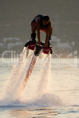 Flyboarder crouching to grab board at dusk