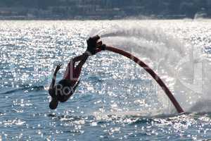 Flyboarder diving backwards headfirst into backlit sea