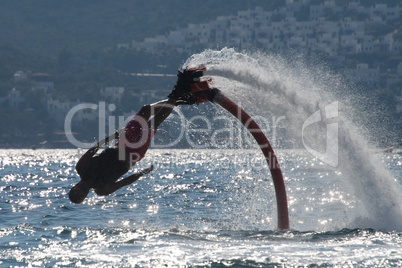 Flyboarder diving diagonally headfirst into backlit waves