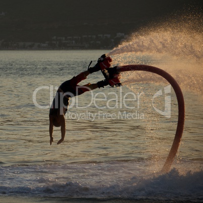 Flyboarder diving followed by backlit water jet