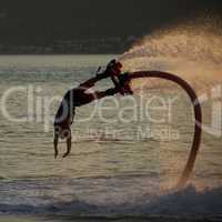 Flyboarder diving followed by backlit water jet