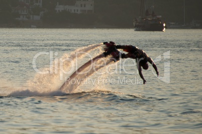 Flyboarder diving into waves with yacht behind