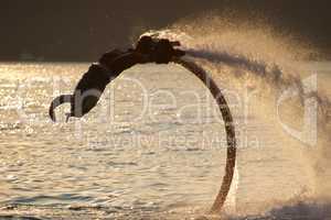 Flyboarder doing back flip over backlit waves