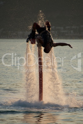 Flyboarder doing back flip surrounded by spray