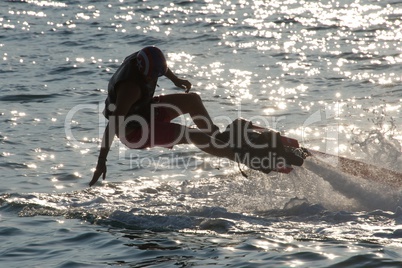 Flyboarder falling over backwards into backlit waves