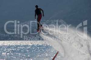 Flyboarder followed by spray over backlit sea