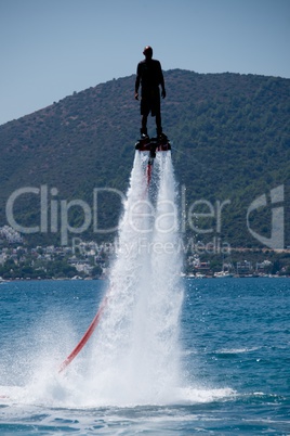 Flyboarder in black silhouetted against wooded hillside