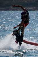 Flyboarder in helmet diving into backlit waves