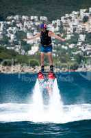 Flyboarder with arms out and village behind