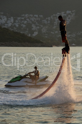 Flyboarder with arms outstretched beside Jet Ski