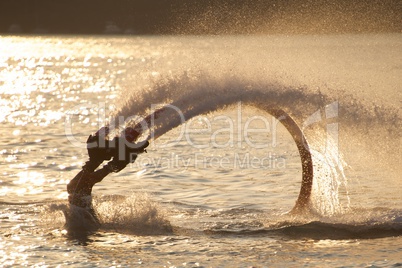 Flyboarder with legs disappearing into backlit sea