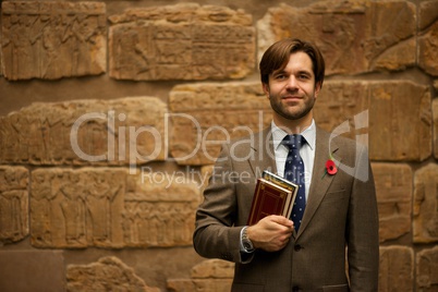 Smiling bearded schoolteacher in museum carrying books