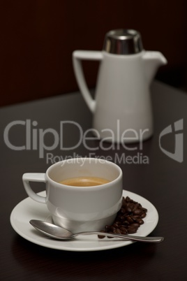 White coffee cup with beans beside pot