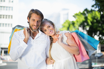 Attractive couple smiling at camera holding bags