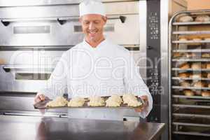 Smiling baker holding tray of raw dough