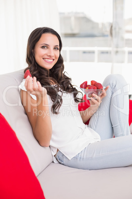 Pretty brunette eating strawberries on couch