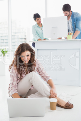 Smiling businesswoman sitting on the floor using laptop