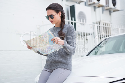 Woman wearing sunglasses reading map beside her car
