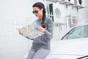 Woman wearing sunglasses reading map beside her car