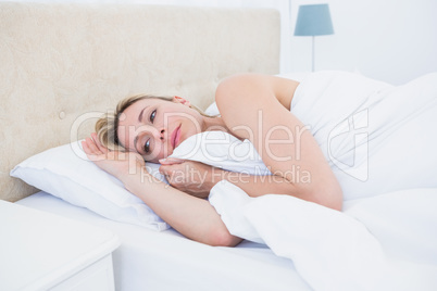 Thoughtful blonde woman lying in bed