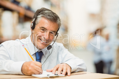 Smiling warehouse manager writing on clipboard