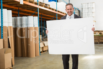 Smiling warehouse manager holding large white poster