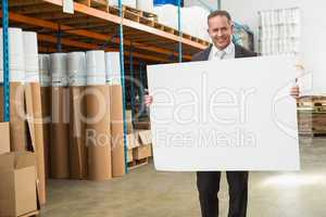 Smiling warehouse manager holding large white poster
