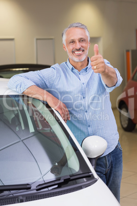 Smiling customer leaning on car while giving thumbs up