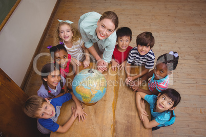 Cute pupils smiling around a globe in classroom with teacher