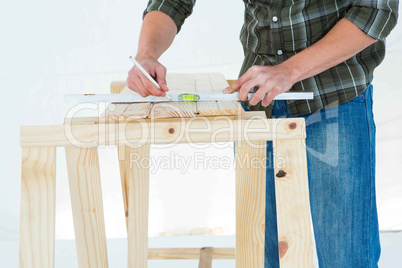 Worker using spirit level to mark on wooden plank