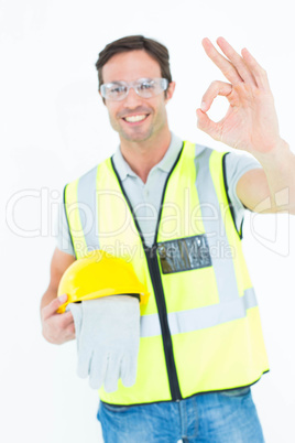 Carpenter holding gloves and hardhat while gesturing OK