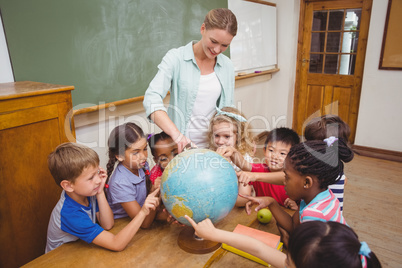 Cute pupils and teacher in classroom with globe