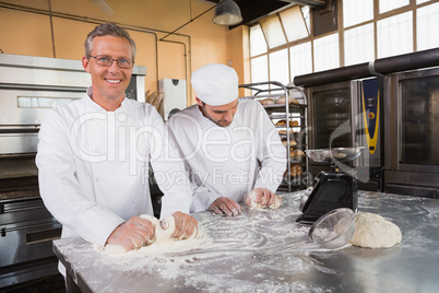 Smiling bakers kneading dough at counter