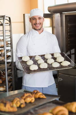 Smiling baker holding tray of raw dough
