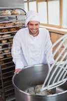 Smiling baker preparing dough in industrial mixer