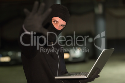 Hacker in balaclava gesturing and using laptop