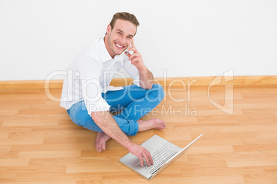 Happy man sitting on floor using laptop at home