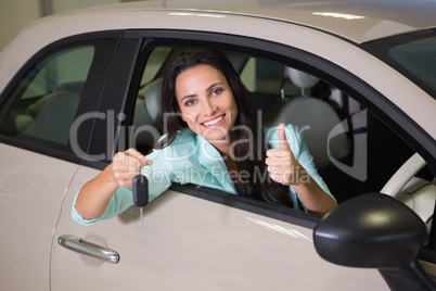Smiling woman holding car key while giving thumbs up