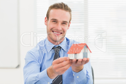 Happy businessman showing miniature house