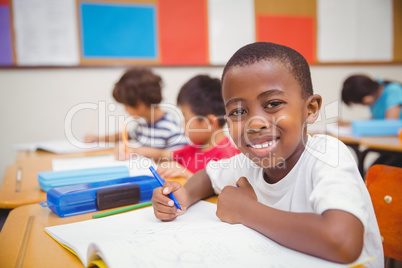 Cute pupils drawing at their desks one smiling at camera