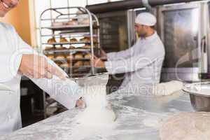 Smiling baker sieving flour on the dough